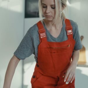 Blonde woman in red overalls sanitizing a wooden table indoors, showcasing home cleaning service.