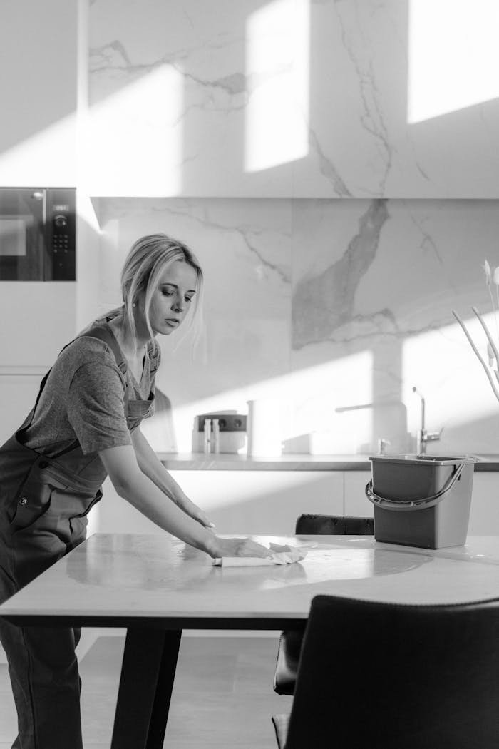about-us A female cleaner sanitizing a kitchen table with natural light casting shadows.