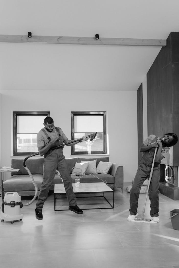 who-we-are Two men clean a modern living room with vacuum and mop, enjoying their work.
