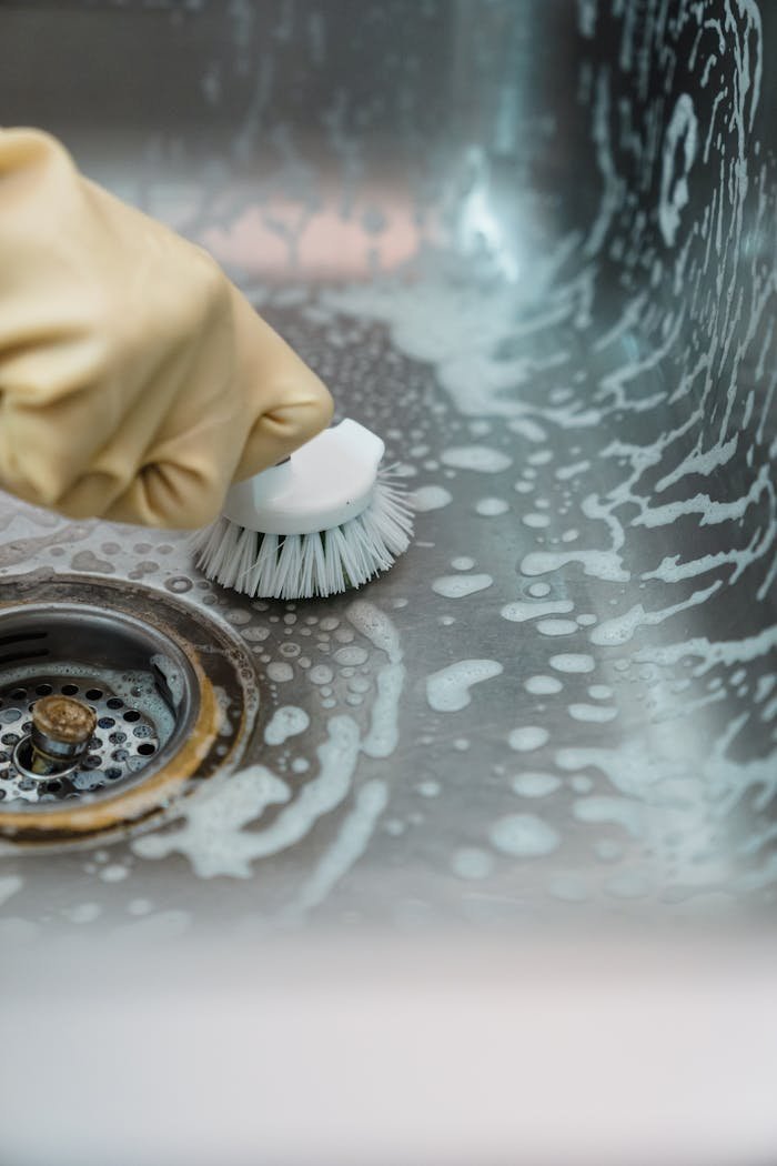 why-choose-us Close-up of a hand in gloves scrubbing a soapy kitchen sink with a brush.